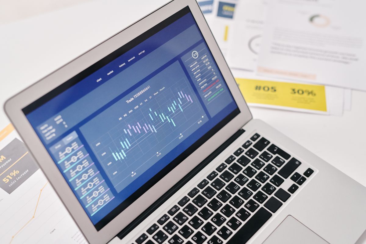 Laptop displaying financial graphs beside reports
